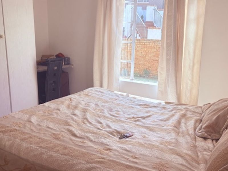 A functional bedroom featuring built-in cupboards and a window providing natural light and views of the exterior brick wall.