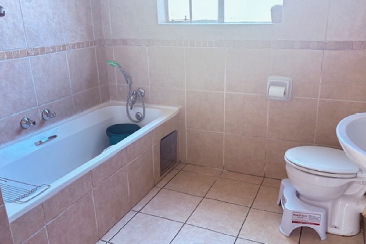 A functional bathroom featuring a built-in bathtub with shower mixer, pedestal basin, and toilet, finished with neutral wall and floor tiling.