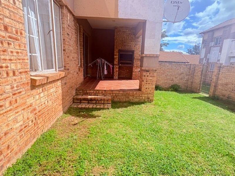 A private rear garden featuring a covered patio with a built-in brick braai, accessible from the main living area of the townhouse.