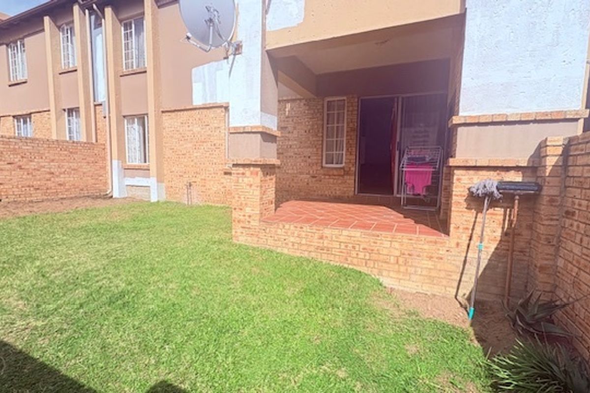 A private rear garden featuring a paved patio area, brick boundary walls, and a small lawn, providing a functional outdoor space for the townhouse.