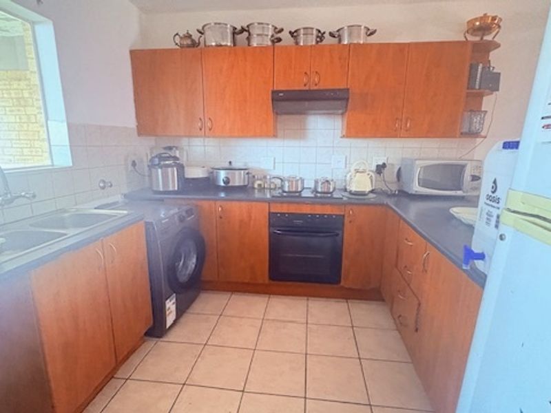 A functional kitchen featuring wooden cabinetry, tiled flooring, a built-in oven, hob, and extractor fan with a double sink and tiled splashback.