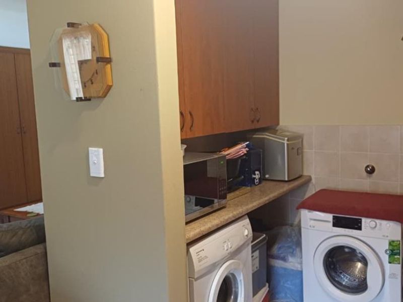 A functional laundry area featuring built-in cabinetry, laminate countertops, and tiled splashback, providing dedicated space for washing appliances and utility storage.