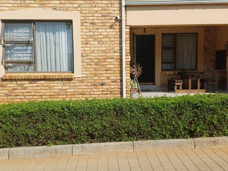 Front elevation of a townhouse featuring a face brick facade, aluminium window frames, and a covered patio area with a built-in braai.