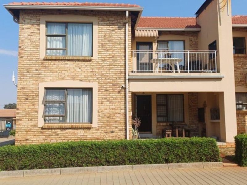 A two-storey townhouse featuring a face-brick facade, a tiled roof, and a private balcony with metal railings, set within a well-maintained complex.