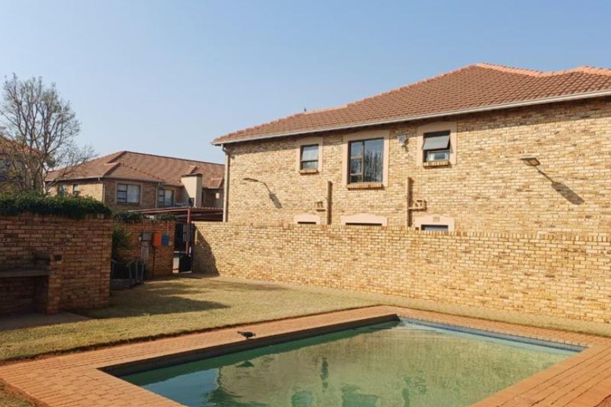 Rear exterior view of the townhouse featuring a private swimming pool, a built-in braai area, and a secure facebrick boundary wall.