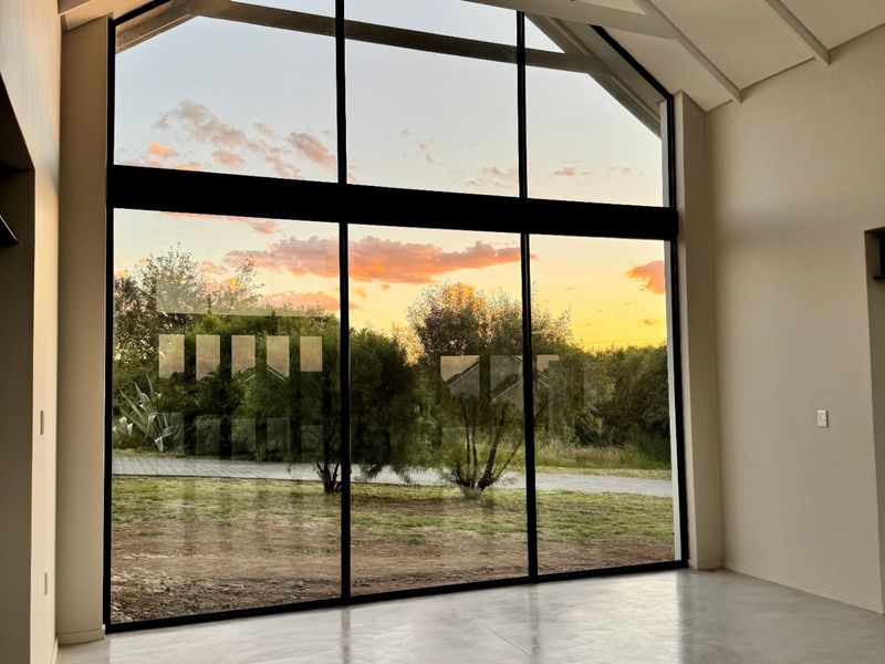 Spacious living area featuring a dramatic vaulted ceiling with exposed rafters, polished concrete floors, and expansive floor-to-ceiling windows offering scenic sunset views.