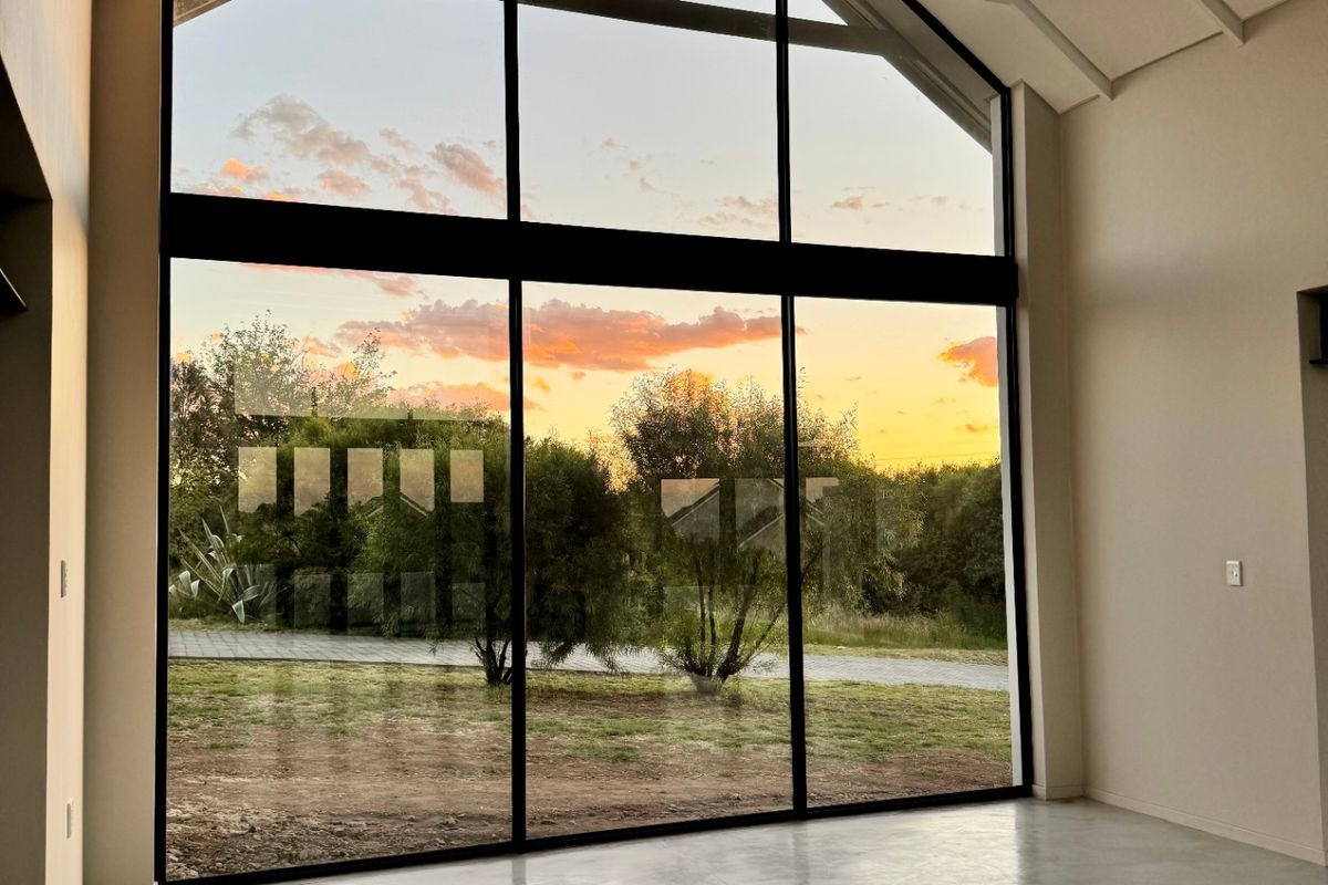 Spacious living area featuring a dramatic vaulted ceiling with exposed rafters, polished concrete floors, and expansive floor-to-ceiling windows offering scenic sunset views.