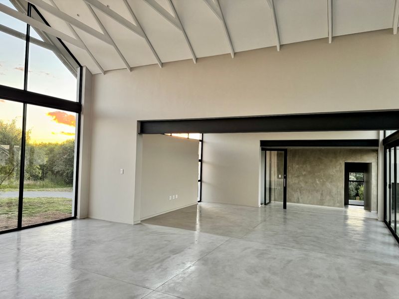 Spacious open-plan living area featuring high vaulted ceilings, polished concrete floors, and expansive floor-to-ceiling windows with modern industrial steel beam accents.