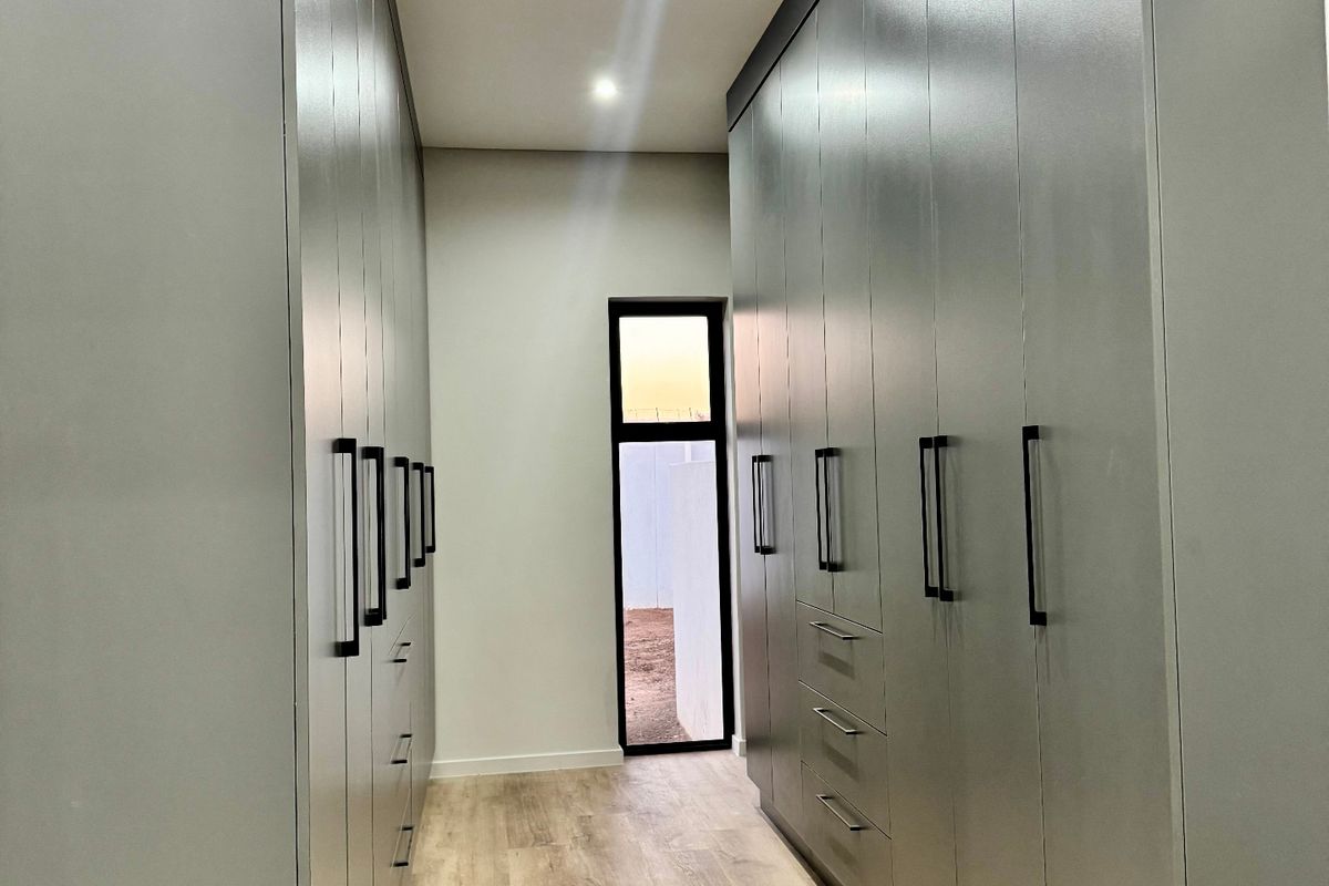 A modern walk-in dressing area featuring extensive floor-to-ceiling built-in cabinetry, recessed lighting, and light wood-look laminate flooring.