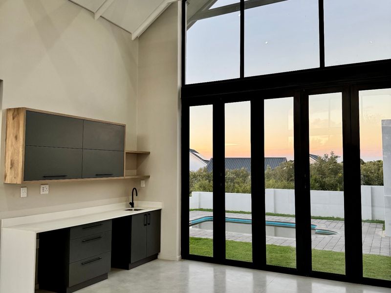 Modern open-plan living space featuring high vaulted ceilings, polished concrete floors, and expansive glass doors opening to a private pool area.