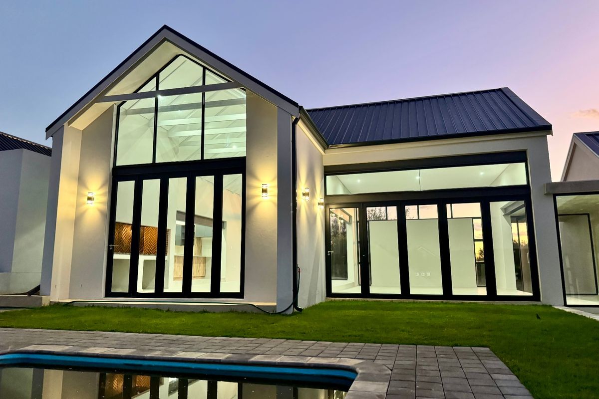 Modern rear elevation featuring a gabled roof, expansive glass doors, integrated wall lighting, and a paved patio area overlooking a swimming pool.