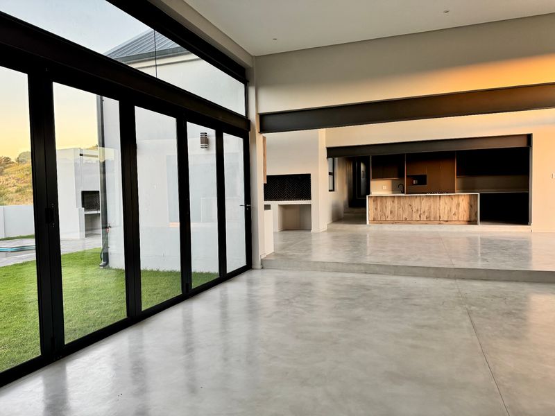Spacious open-plan living area featuring polished concrete floors, exposed steel beams, and large bi-fold doors opening to the garden.