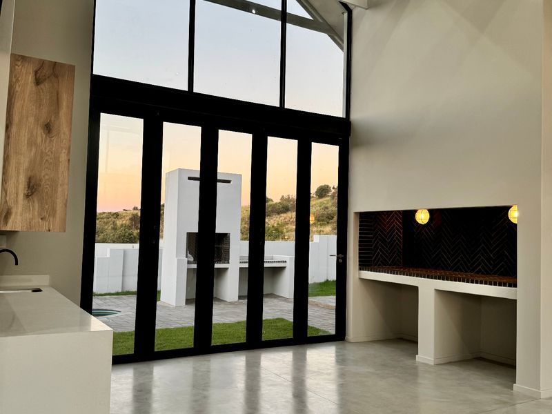 Spacious open-plan living area featuring vaulted ceilings, polished concrete floors, and large bi-fold doors opening to an outdoor entertainment space with a built-in braai.