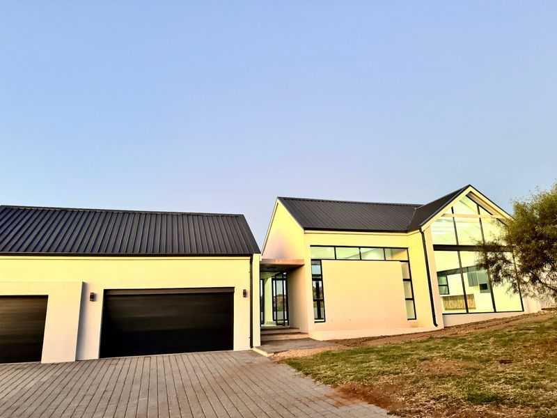 Modern architectural home featuring a double garage, metal roofing, and expansive glass windows, set on a paved driveway with a clean, contemporary facade.