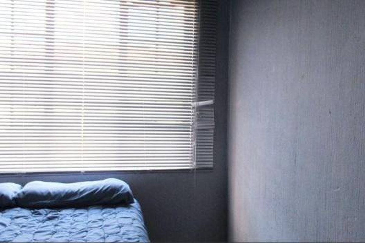 A bedroom featuring a window with horizontal blinds and textured wall finishes.