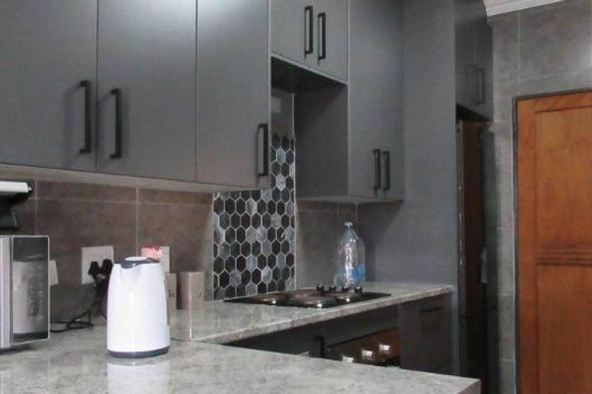 Modern kitchen featuring dark grey cabinetry, stone-look countertops, and a distinctive hexagonal tile backsplash, complemented by a solid timber door.