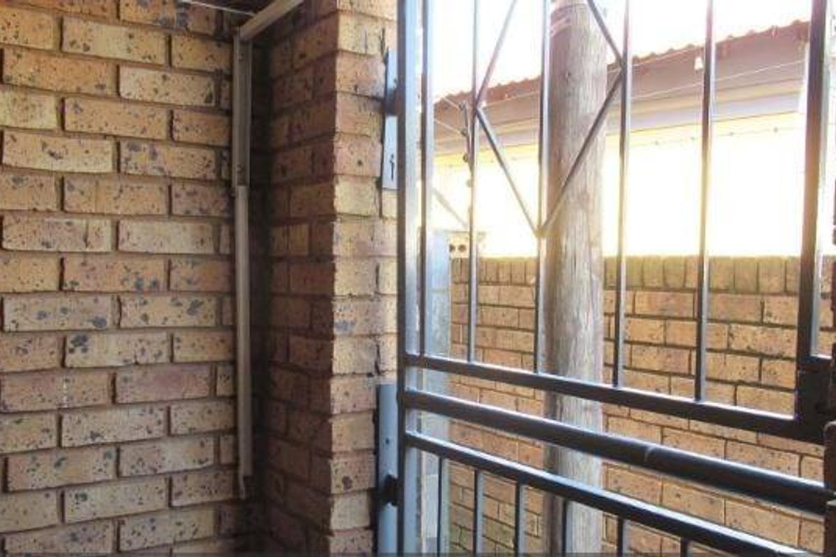 A view of an exterior brick wall and a metal security gate, showing the property's structural perimeter and security features.
