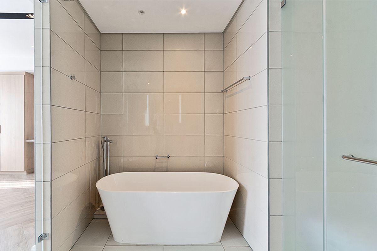 A modern, minimalist bathroom featuring a sleek freestanding bathtub, neutral floor-to-ceiling wall tiles, and recessed lighting.
