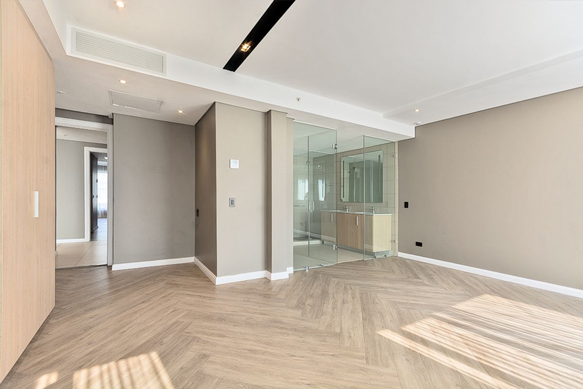 Spacious bedroom featuring modern herringbone wood flooring, built-in cabinetry, and a sleek glass-enclosed en-suite bathroom with contemporary finishes.