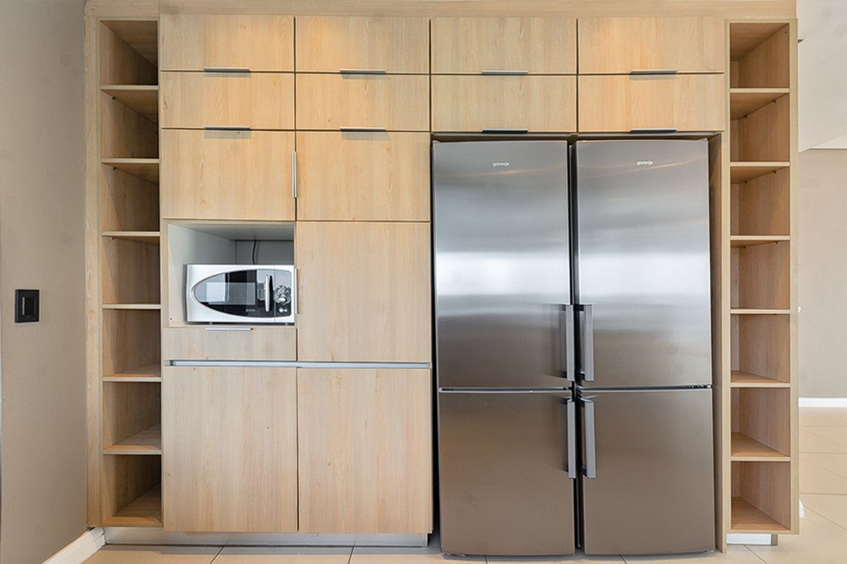 A modern kitchen wall featuring light wood cabinetry, integrated microwave, and a large stainless steel double-door refrigerator with ample open shelving.