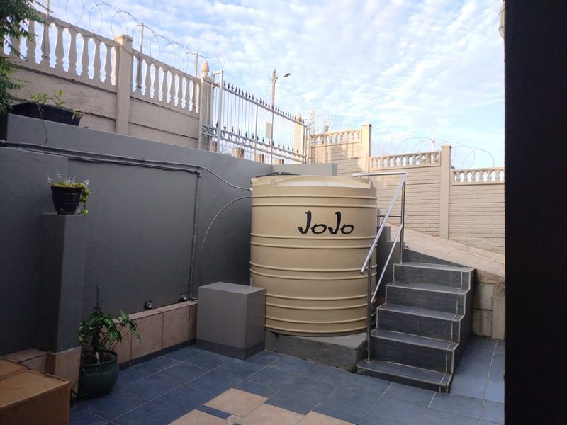 Rear exterior area featuring a water storage tank, tiled staircase with stainless steel handrail, and secure perimeter walling.