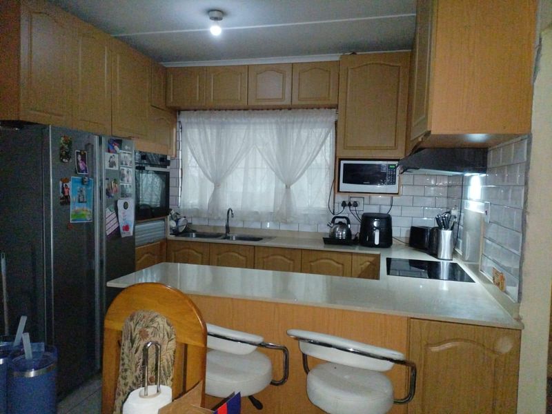 A functional kitchen featuring wood-finish cabinetry, a breakfast bar, subway tile backsplash, and integrated appliances including an oven and hob.