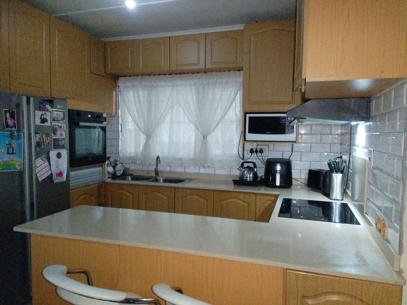 A functional kitchen featuring wood-finish cabinetry, subway tile backsplash, integrated oven, electric hob, and a breakfast bar counter.