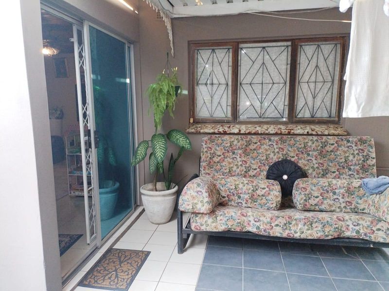 A covered patio area featuring tiled flooring, a sliding glass door with security gate, and windows fitted with security bars.