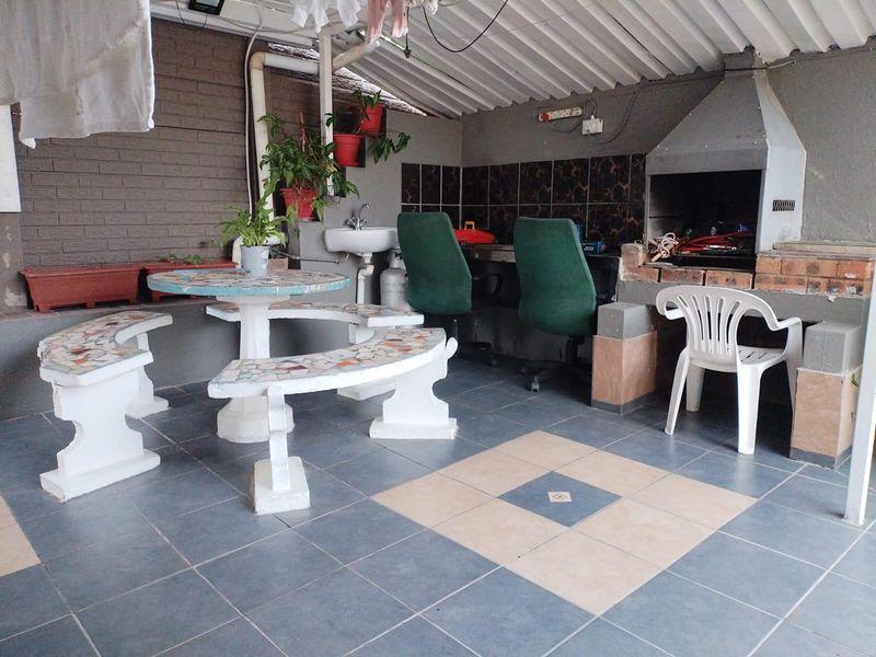 Covered outdoor patio area featuring a built-in braai, tiled flooring, and a wall-mounted basin, providing a functional space for outdoor entertaining.