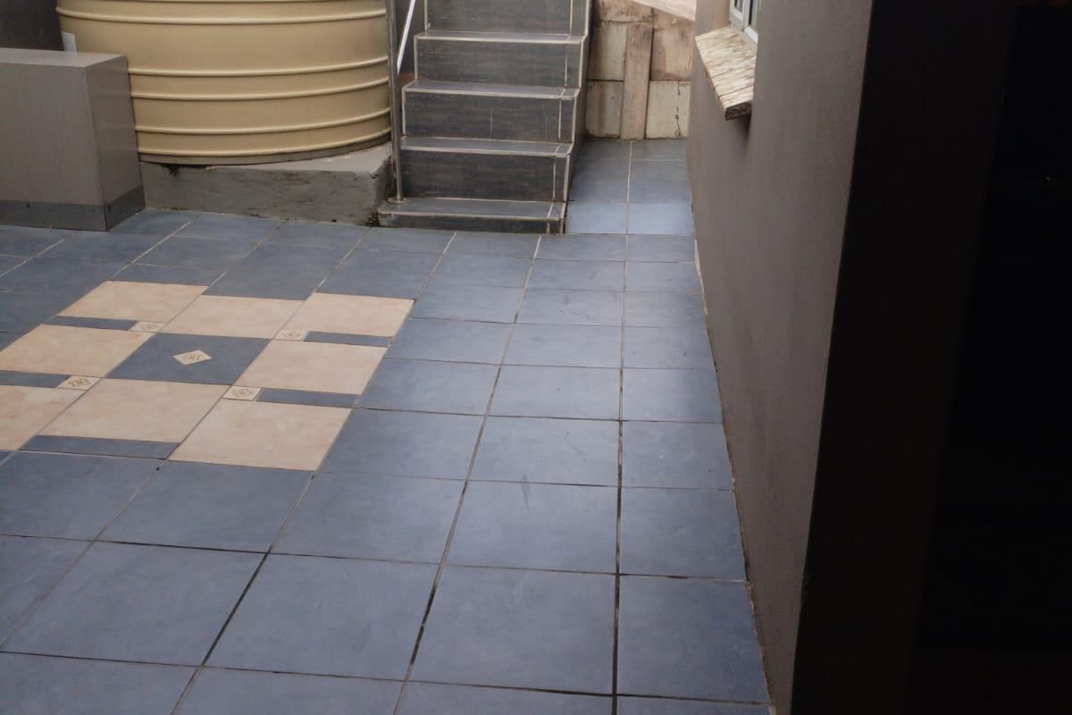 A paved rear courtyard area featuring a large water storage tank, external staircase with metal handrail, and perimeter boundary walling.