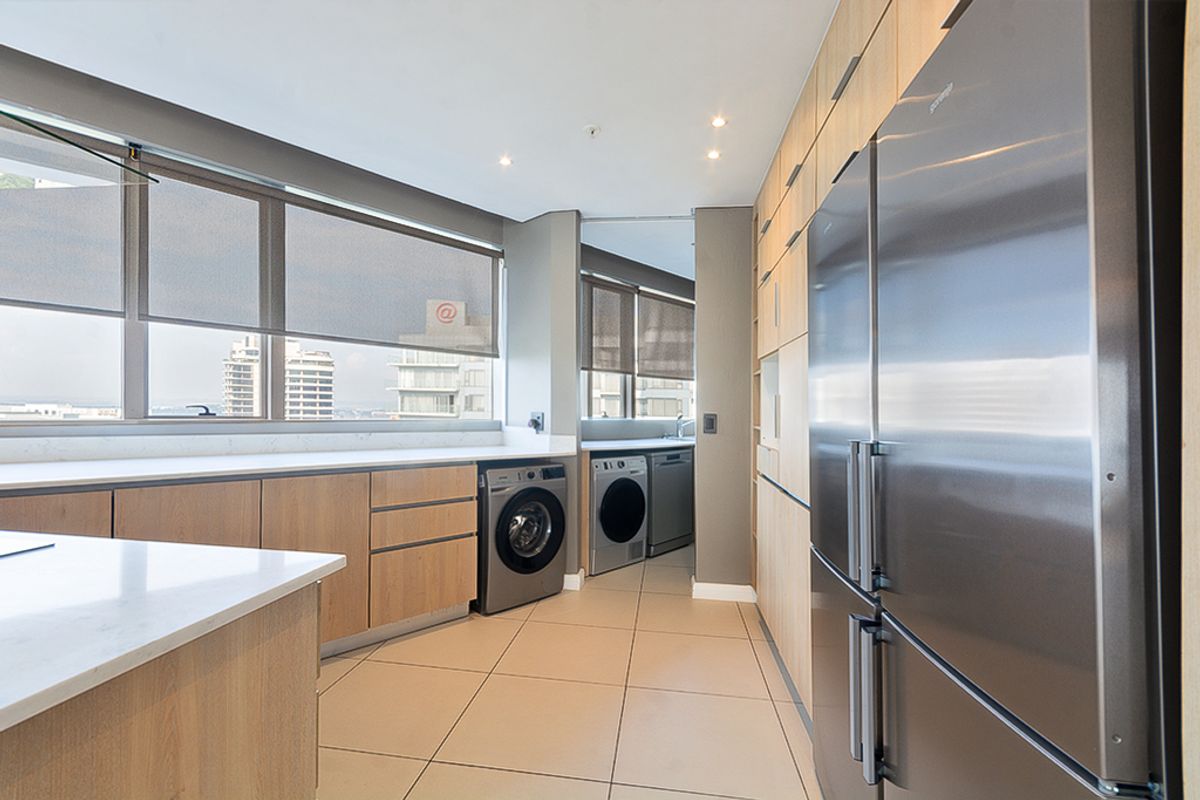 Modern kitchen featuring light wood cabinetry, stone countertops, integrated appliances, and large windows with roller blinds, offering a clean and functional workspace.