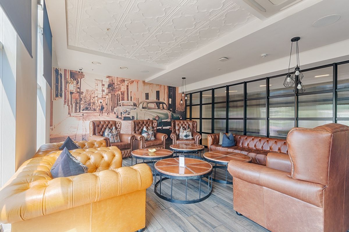 A well-appointed lounge area featuring decorative ceiling tiles, recessed lighting, and a modern glass partition wall, finished with durable wood-look tile flooring.
