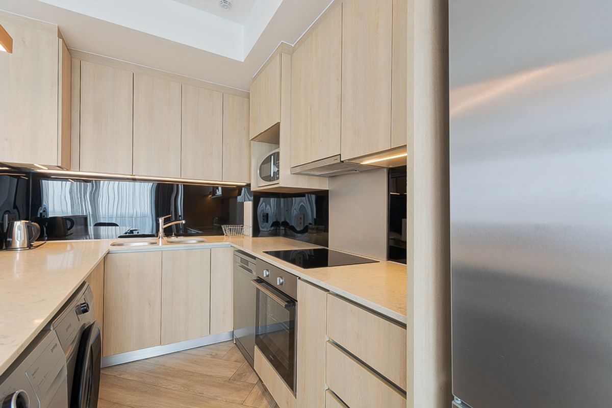 Modern kitchen featuring light wood cabinetry, stone countertops, black glass splashback, and integrated appliances including an oven, hob, and microwave.