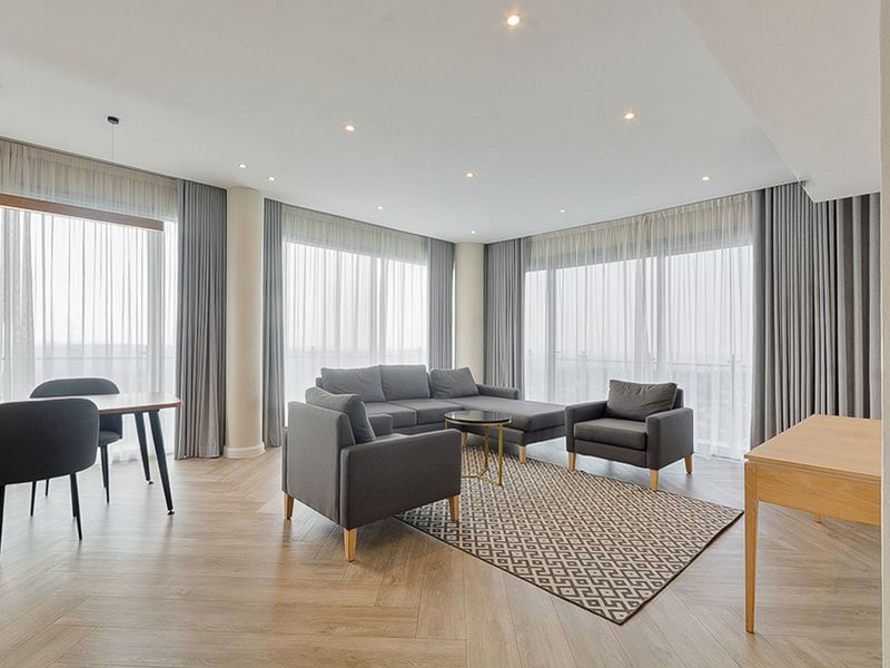 Spacious open-plan living and dining area featuring herringbone timber flooring, floor-to-ceiling windows with integrated curtain tracks, and modern recessed downlighting.