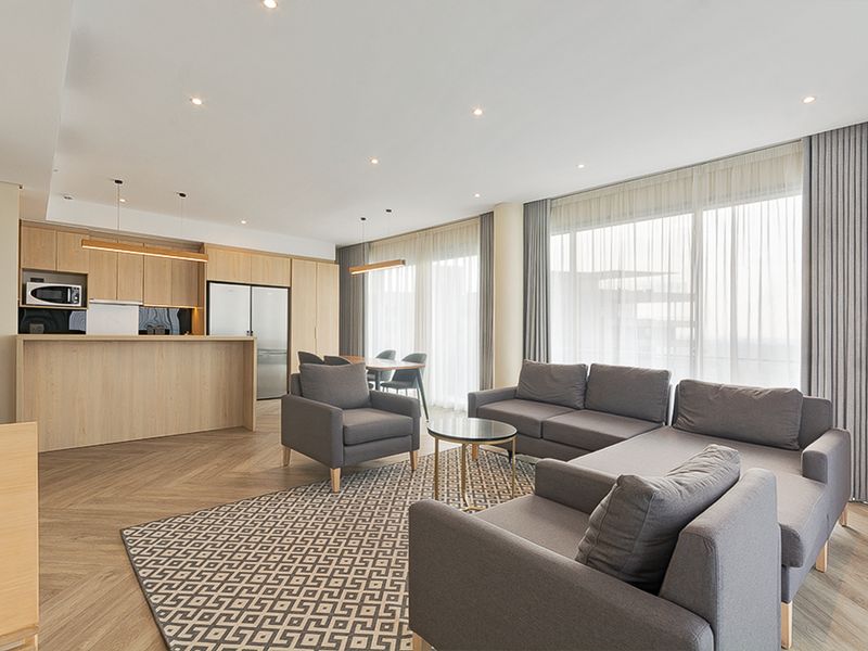 Modern open-plan living area featuring a sleek integrated kitchen with light wood cabinetry, herringbone flooring, and expansive floor-to-ceiling windows with sheer curtains.