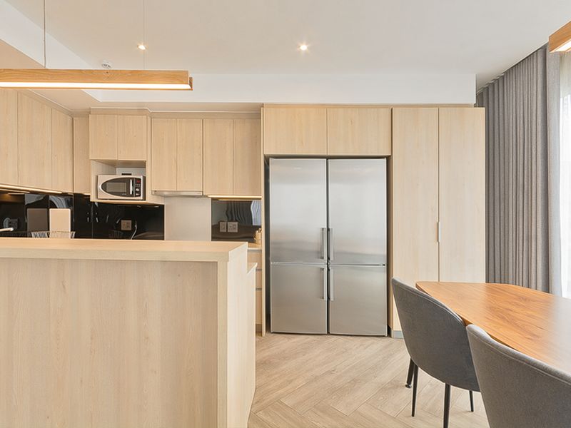 Modern open-plan kitchen featuring light-wood cabinetry, integrated appliances, a breakfast bar, and stylish herringbone flooring in a bright, contemporary living space.