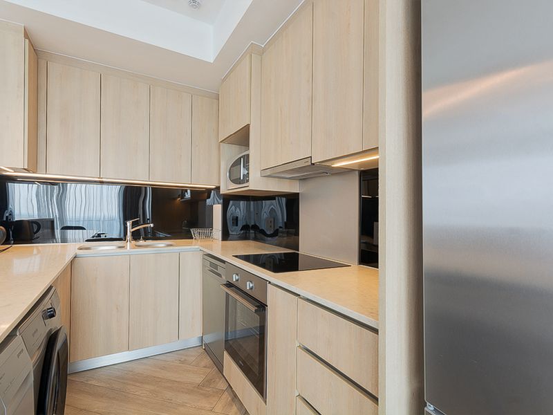 Modern kitchen featuring light wood cabinetry, stone countertops, black glass splashback, and integrated appliances including an oven, hob, and microwave.