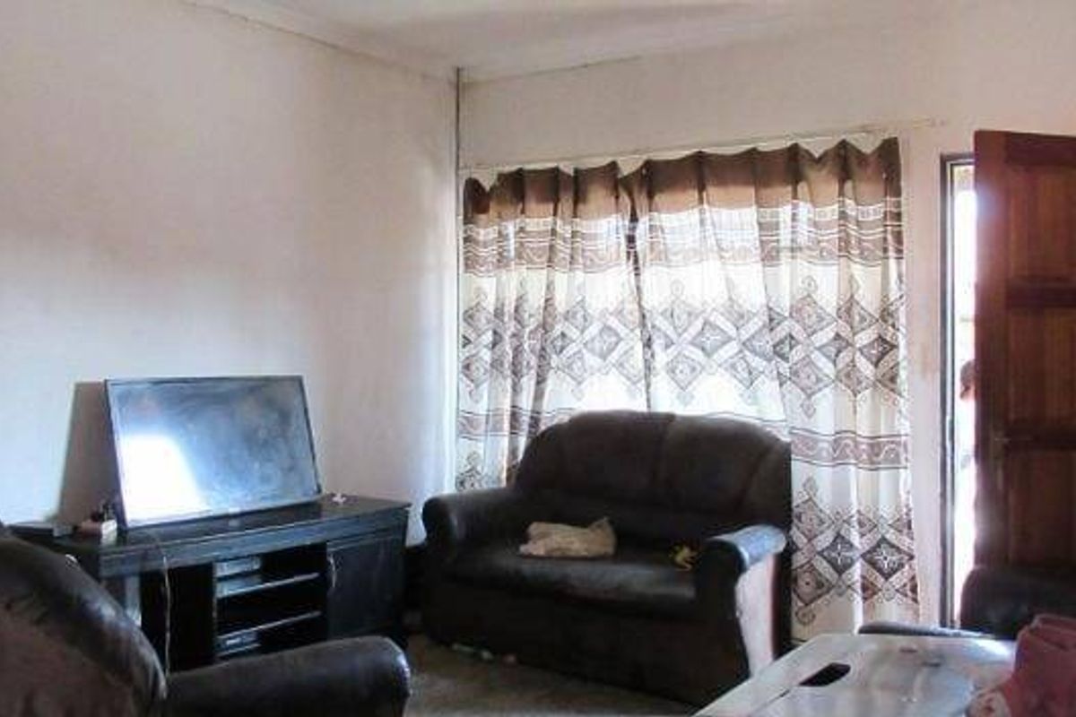 A living room area featuring a wooden entrance door and large window with curtains, providing natural light to the space.