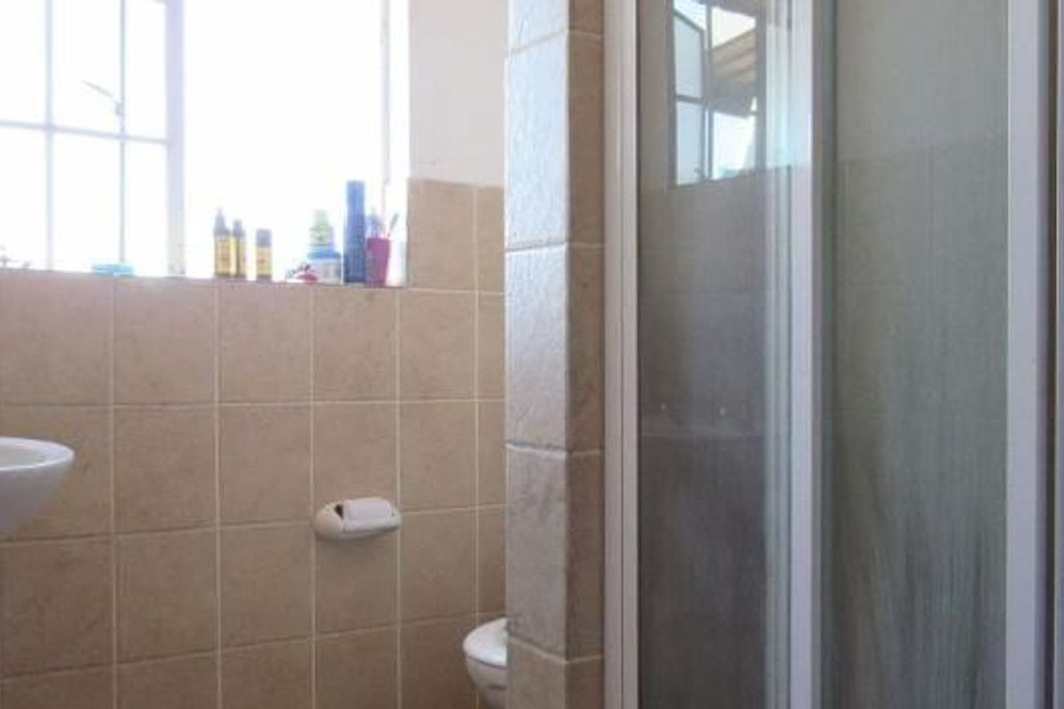 A functional bathroom featuring a pedestal basin, a shower enclosure with a glass door, and neutral wall tiling.