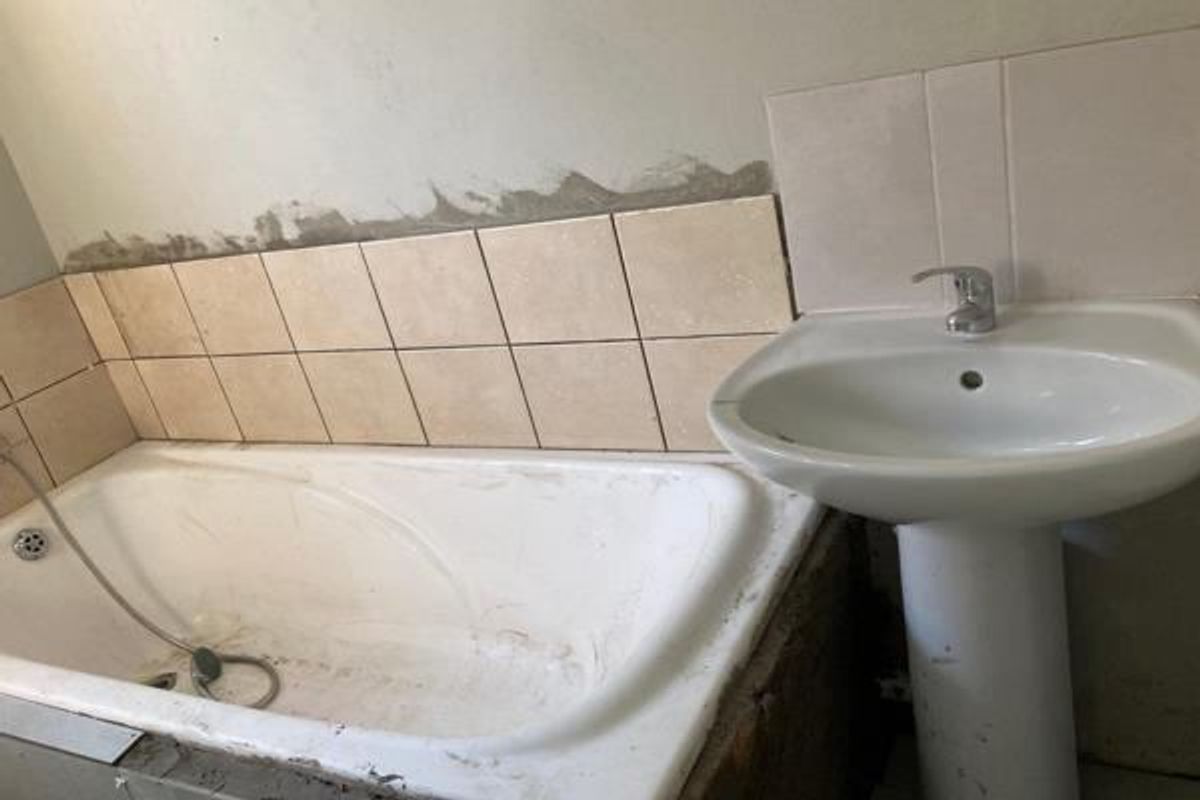 A bathroom in need of renovation, featuring a pedestal basin and built-in bathtub with unfinished wall tiling and exposed structural elements.