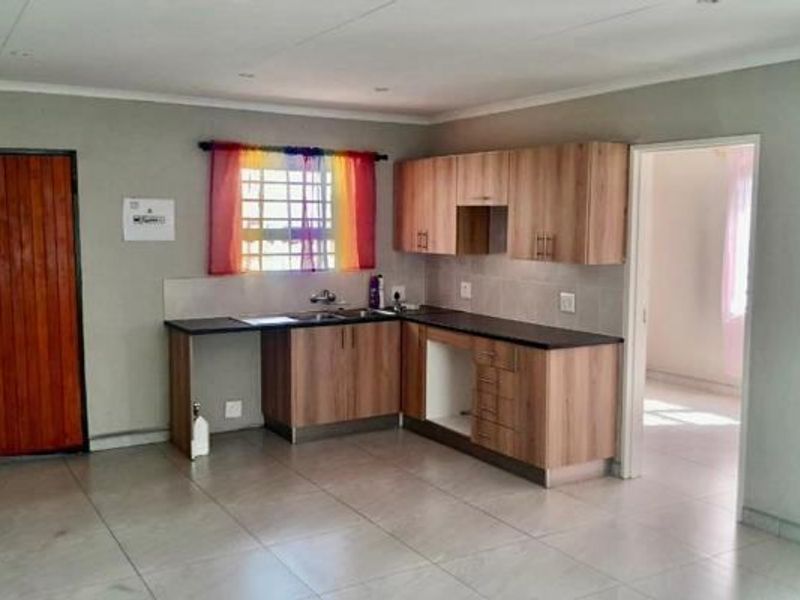 A functional kitchen featuring laminate cabinetry, dark countertops, a stainless steel sink, and tiled flooring, offering a clean and practical workspace.