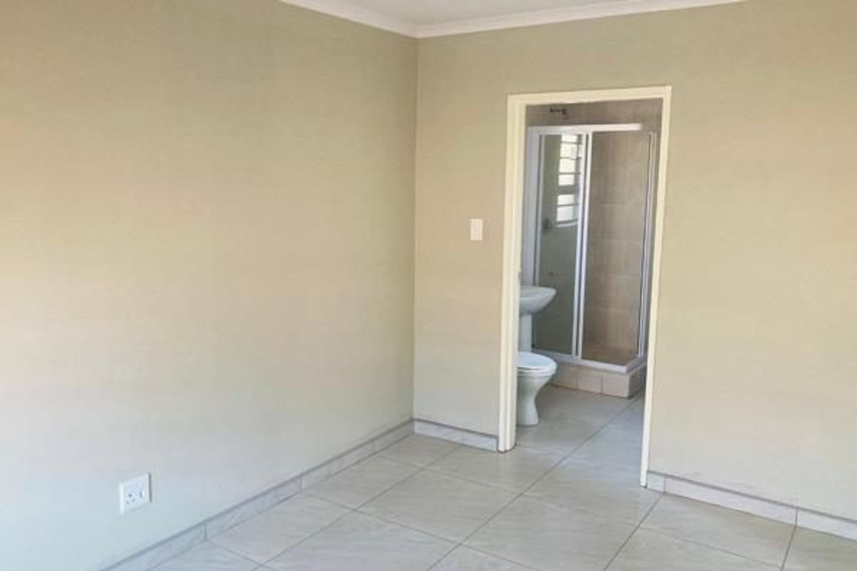 A clean, empty bedroom featuring neutral tiled flooring and direct access to an en-suite bathroom with a shower.