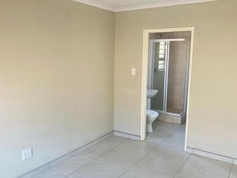 A clean, empty bedroom featuring neutral tiled flooring and direct access to an en-suite bathroom with a shower.