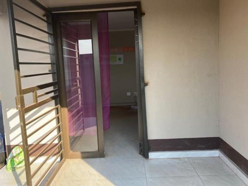 A covered entrance area featuring a security gate, aluminium framed door, and tiled flooring, providing access to the interior living space.
