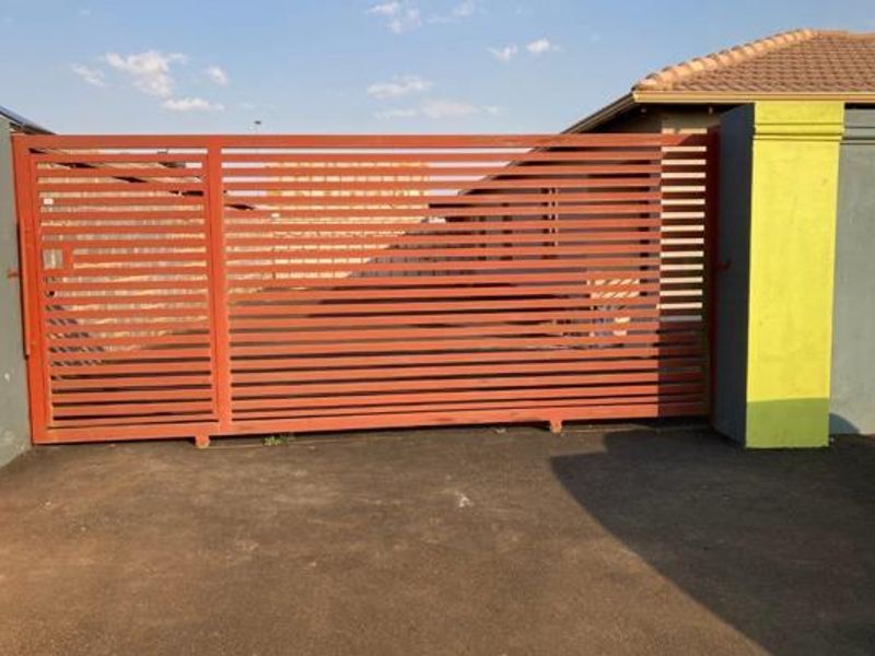 Front view of the property featuring a modern horizontal slat sliding gate, paved driveway, and perimeter boundary walls.