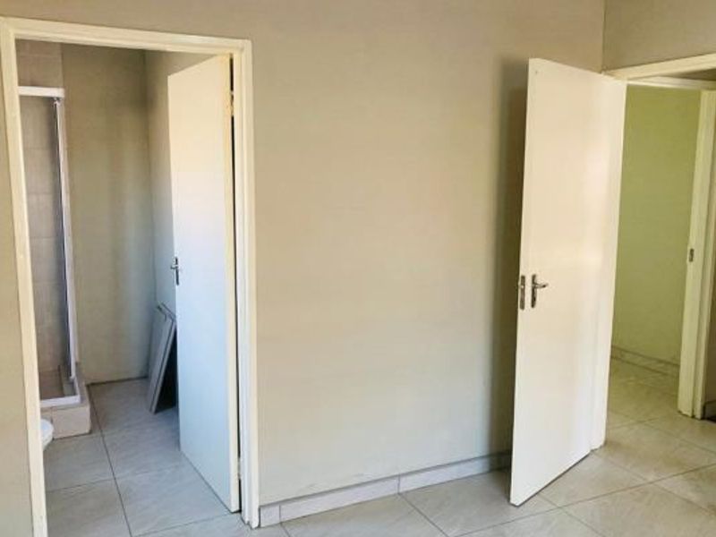 A neutral hallway area featuring tiled flooring and access to adjacent rooms, including a bathroom with a shower enclosure.