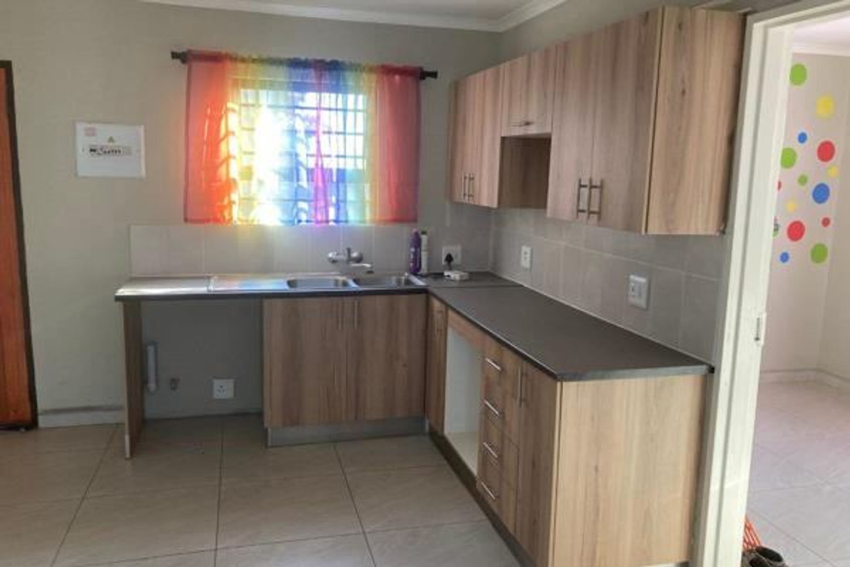 A functional kitchen featuring light wood-tone cabinetry, dark laminate countertops, tiled splashbacks, and ceramic floor tiles, offering a clean and practical workspace.