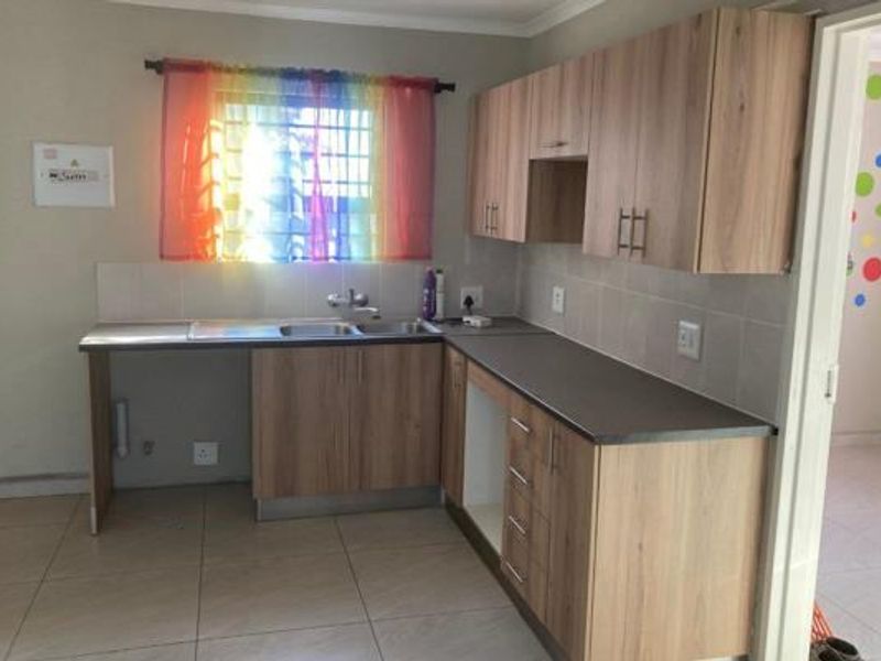 A functional kitchen featuring light wood-tone cabinetry, dark laminate countertops, tiled splashbacks, and ceramic floor tiles, offering a clean and practical workspace.