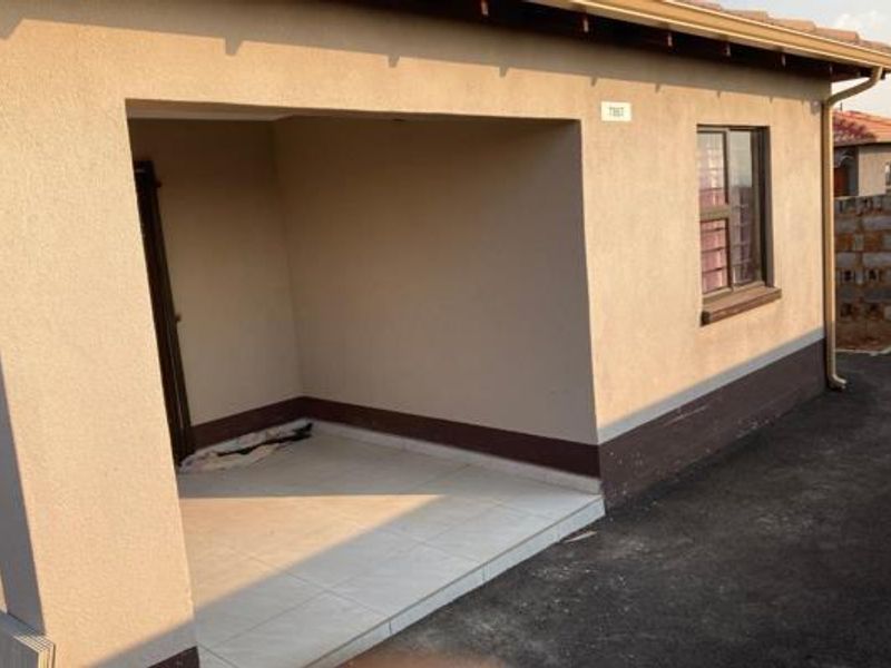 A covered patio area featuring tiled flooring and plastered exterior walls, providing a functional outdoor space adjacent to the main building structure.