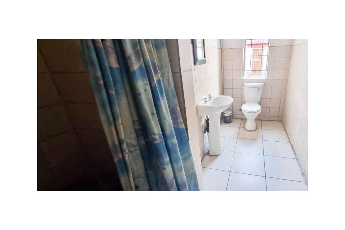 A functional bathroom featuring a pedestal basin, toilet, and tiled finishes throughout, including a shower area with a curtain.